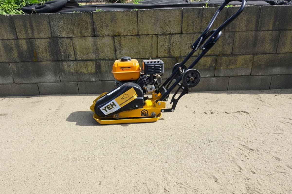 A yellow and black YEH brand plate compactor with a gasoline engine, positioned outdoors on a paved surface with a stone wall in the background.